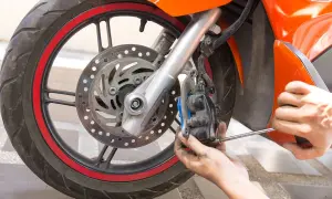 Mecánico ajustando el freno delantero de una motocicleta naranja. Se ve la rueda, el disco y la pinza.
