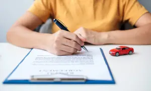Persona firma un documento, quizás para saber como dar de baja un seguro de coche. Un coche rojo en miniatura está al lado.