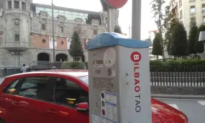 Máquina de parquímetro con el logo de BILBAO TAO en una calle de Bilbao. Un coche rojo está aparcado al lado.