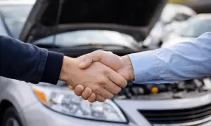 Dos hombres se dan la mano frente a un coche con el capó abierto. Un acuerdo sellado, el tfsi significado de una transacción exitosa.