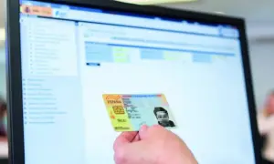 Mano sostiene DNI español frente a pantalla de ordenador con interfaz de apoderamiento DGT.