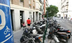 Señal azul de normativa aparcamiento motos. Calle con muchas motos aparcadas y un padre con su hija caminando.