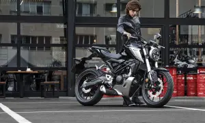 Joven con chaqueta de cuero junto a una moto negra. ¡Si te sacas el carnet de coche puedes conducir moto!