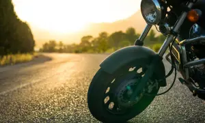 Rueda delantera de una motocicleta en una carretera al atardecer. La tija de la moto se ve claramente, lista para el viaje.
