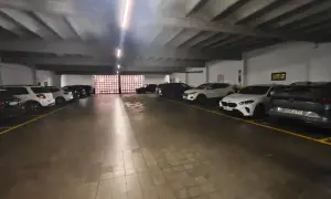 Coches aparcados en diagonal en un garaje subterráneo con iluminación fluorescente y suelo de baldosas.