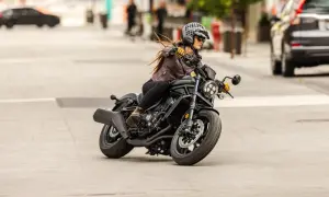 Mujer con casco y chaqueta de cuero conduce una motocicleta negra. Sorprendentemente, una motocicleta puede circular sin tubo de escape, demostrando su potencia.