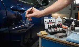 Persona aplica pintura con pincel para reparar arañazos coche. Kit de retoque, pulidora y alcohol isopropílico a la vista.