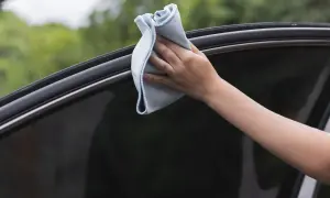 Mano limpiando el cristal del coche con un paño azul. Aprende como limpiar los cristales del coche para que queden perfectos y sin marcas.