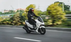 Persona con casco y chaqueta negra conduce una moto blanca. La edad para conducir moto de 125cc es 16 años.