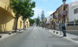 Calle soleada en zbe Fuengirola con casas blancas y amarillas, árboles verdes y bolardos de hormigón.