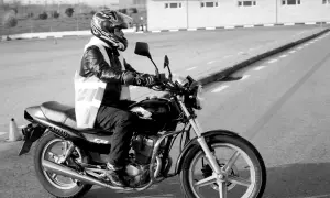 Motociclista con casco y chaleco reflectante en un circuito, preparándose para un test am dgt.