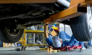Mecánico trabajando bajo un coche elevado, intentando arreglar por qué no entran las marchas.