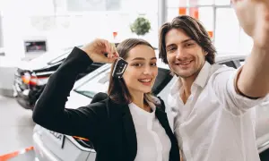 Pareja feliz celebrando la compra de un coche nuevo, ella muestra las llaves. ¡Ya pueden poner el coche a nombre de dos personas!
