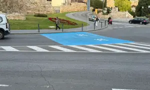 Paso de peatones azul en la zona bajas emisiones de Tarragona, con restos arqueológicos al fondo.