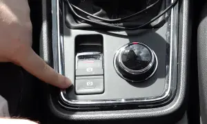 Dedo presionando el botón de freno de mano electrónico en un coche. Esto es útil para entender qué significa "hold" en un coche, ya que activa el freno automático.