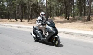 Hombre con casco conduce moto Peugeot con carnet B por carretera rodeada de pinos.