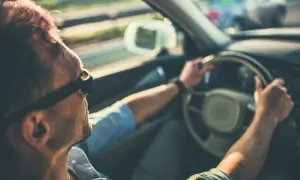 Hombre con gafas de sol conduce, notando que mi coche vibra a partir de 100 km/h. El sol ilumina su cabello.