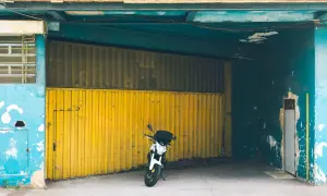 Una moto blanca espera en una cochera con puerta amarilla, donde se puede aparcar sin vado.