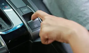 Dedo presionando el botón del freno de estacionamiento eléctrico, junto a la palanca de cambios.