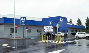 Edificio azul y gris de **itv extraordinaria** con señales de tráfico y coches aparcados en un día lluvioso.