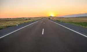 Una carretera convencional se extiende hacia el horizonte bajo un atardecer dorado.