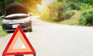Triángulo de emergencia rojo en el arcén. El capó de un coche está abierto, indicando una avería.