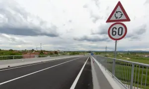 Señal de tráfico indica velocidad minima en carretera convencional de 60 km/h, con un cruce de rotonda cercano.