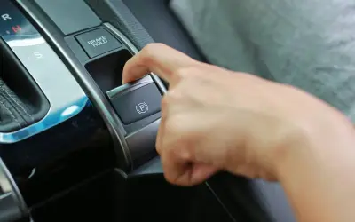 Dedo presionando el botón del freno de estacionamiento eléctrico, junto a la palanca de cambios.
