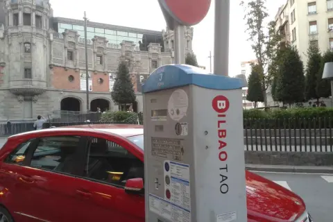 Máquina de parquímetro con el logo de BILBAO TAO en una calle de Bilbao. Un coche rojo está aparcado al lado.