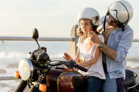 Un padre ayuda a su hija a ponerse el casco para un paseo en moto. Ambos llevan cascos blancos.