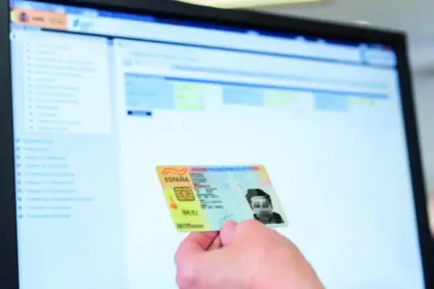 Mano sostiene DNI español frente a pantalla de ordenador con interfaz de apoderamiento DGT.