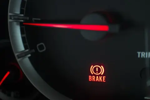 El panel de un coche muestra una luz de advertencia roja con un signo de exclamación dentro de un círculo y la palabra "BRAKE". Esto indica que algo no va bien con el sistema de frenos.