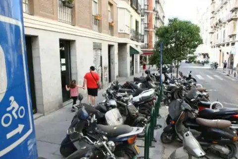 Señal azul de normativa aparcamiento motos. Calle con muchas motos aparcadas y un padre con su hija caminando.