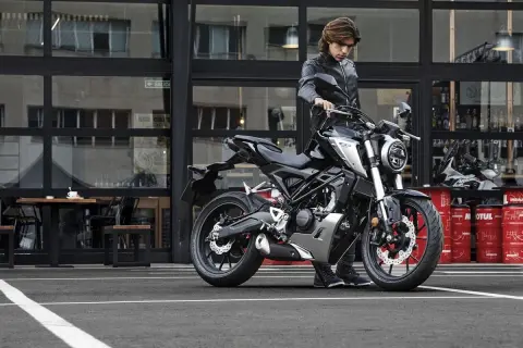 Joven con chaqueta de cuero junto a una moto negra. ¡Si te sacas el carnet de coche puedes conducir moto!