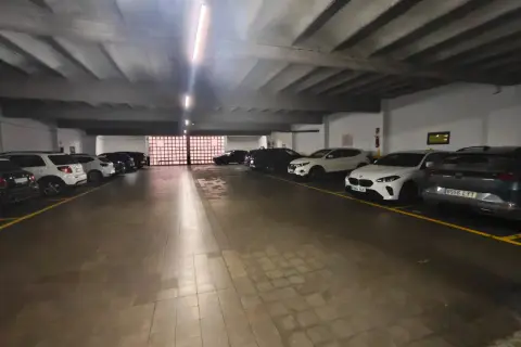 Coches aparcados en diagonal en un garaje subterráneo con iluminación fluorescente y suelo de baldosas.