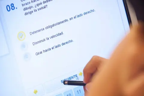 Persona realizando el test DGT A1 en una pantalla táctil. La pregunta 8, con una opción marcada, se centra en la señalización.
