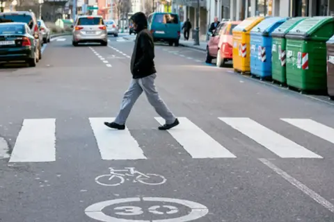 Un hombre cruza la calle por un paso de cebra. Se considera peatón a la persona que camina, y él está haciendo exactamente eso, respetando las normas de tráfico.