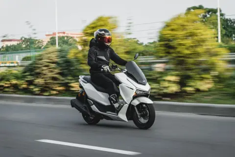 Persona con casco y chaqueta negra conduce una moto blanca. La edad para conducir moto de 125cc es 16 años.