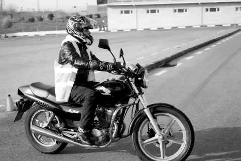 Motociclista con casco y chaleco reflectante en un circuito, preparándose para un test am dgt.