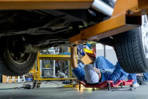 Mecánico trabajando bajo un coche elevado, intentando arreglar por qué no entran las marchas.