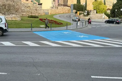 Paso de peatones azul en la zona bajas emisiones de Tarragona, con restos arqueológicos al fondo.