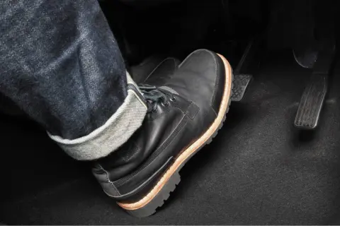 Pie con bota negra pisando el pedal del embrague. Para frenar hay que pisar el embrague y luego el freno.