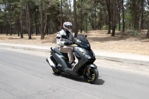 Hombre con casco conduce moto Peugeot con carnet B por carretera rodeada de pinos.