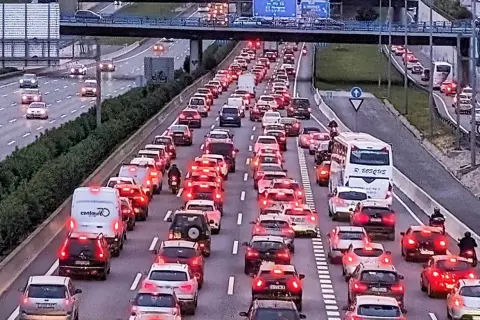 Motociclista aprovecha el atasco para adelantar con moto en autopista congestionada. Coches parados, luces rojas y un autobús blanco.