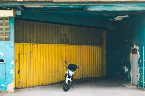 Una moto blanca espera en una cochera con puerta amarilla, donde se puede aparcar sin vado.