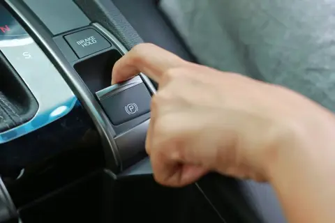 Dedo presionando el botón del freno de estacionamiento eléctrico, junto a la palanca de cambios.