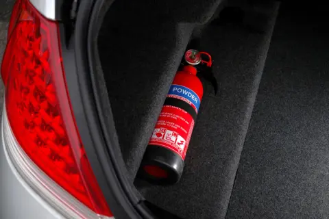 Extintor rojo en el maletero de un coche, listo para emergencias. Es obligatorio llevar extintor en el coche.