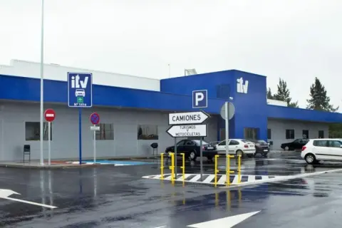 Edificio azul y gris de **itv extraordinaria** con señales de tráfico y coches aparcados en un día lluvioso.
