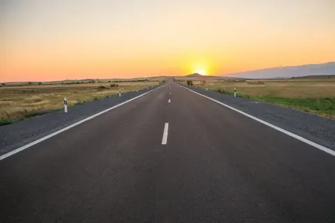 Una carretera convencional se extiende hacia el horizonte bajo un atardecer dorado.