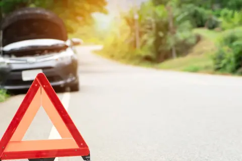 Triángulo de emergencia rojo en el arcén. El capó de un coche está abierto, indicando una avería.